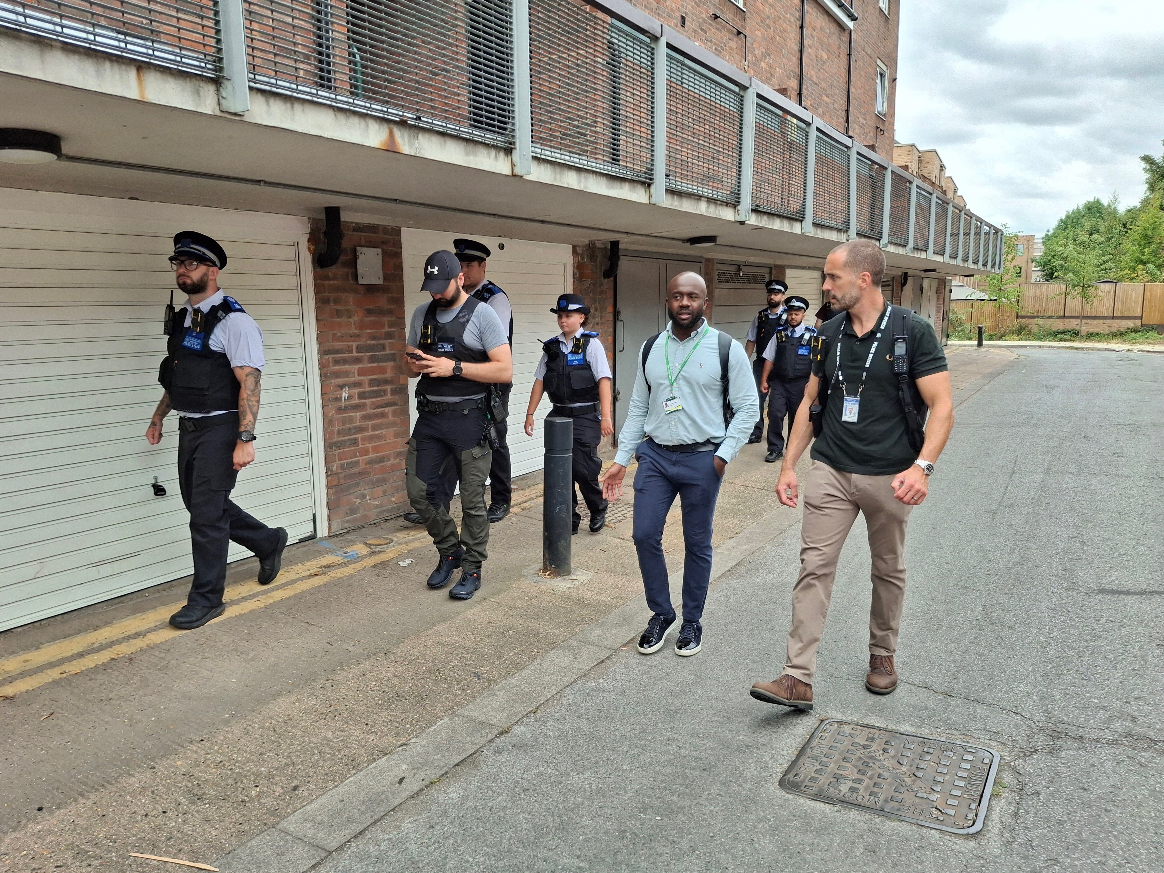 Police patrol walking with Islington Councillor Angelo Weekes next to garage doors under flats on an estate