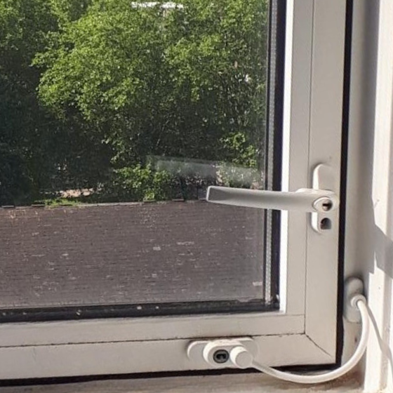 The inside view of a window with a restrictor, two separate hinges joined by a thick wire with one attached to the outer frame vertically and the other to the inner window frame horizontally.